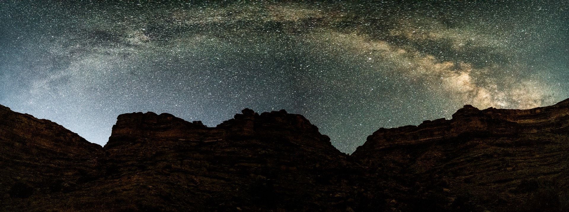 Night sky filled with stars over a dark mountain range. Milky Way visible.