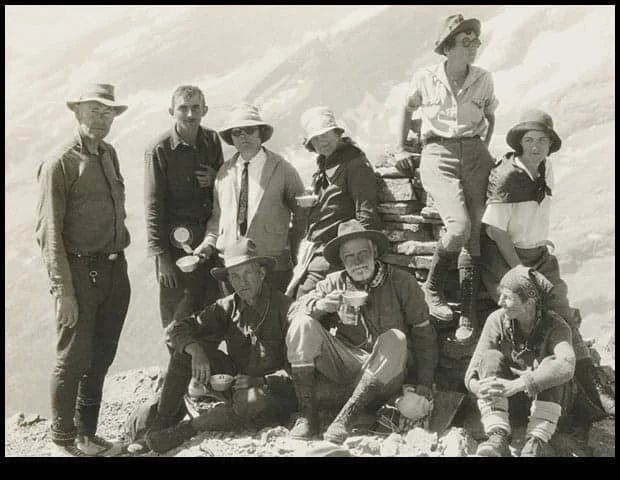 Group of people posing outdoors on a rocky area; some sitting, others standing. All are wearing hats.