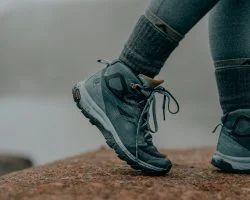 Person wearing gray hiking boots on a rock, with gray jeans and socks.