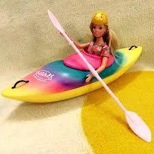 Doll in a kayak with a paddle; rainbow colors, yellow helmet.