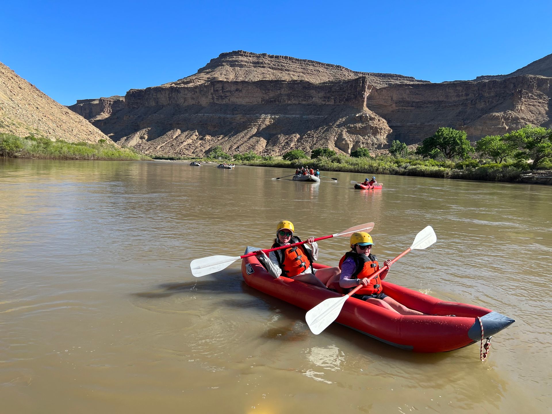 Two people kayaking on a river with a mountain backdrop. Sunny day.