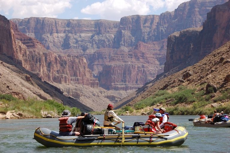 Rafting on a river in a canyon. People in rafts, red cliffs, blue water, sunny day.