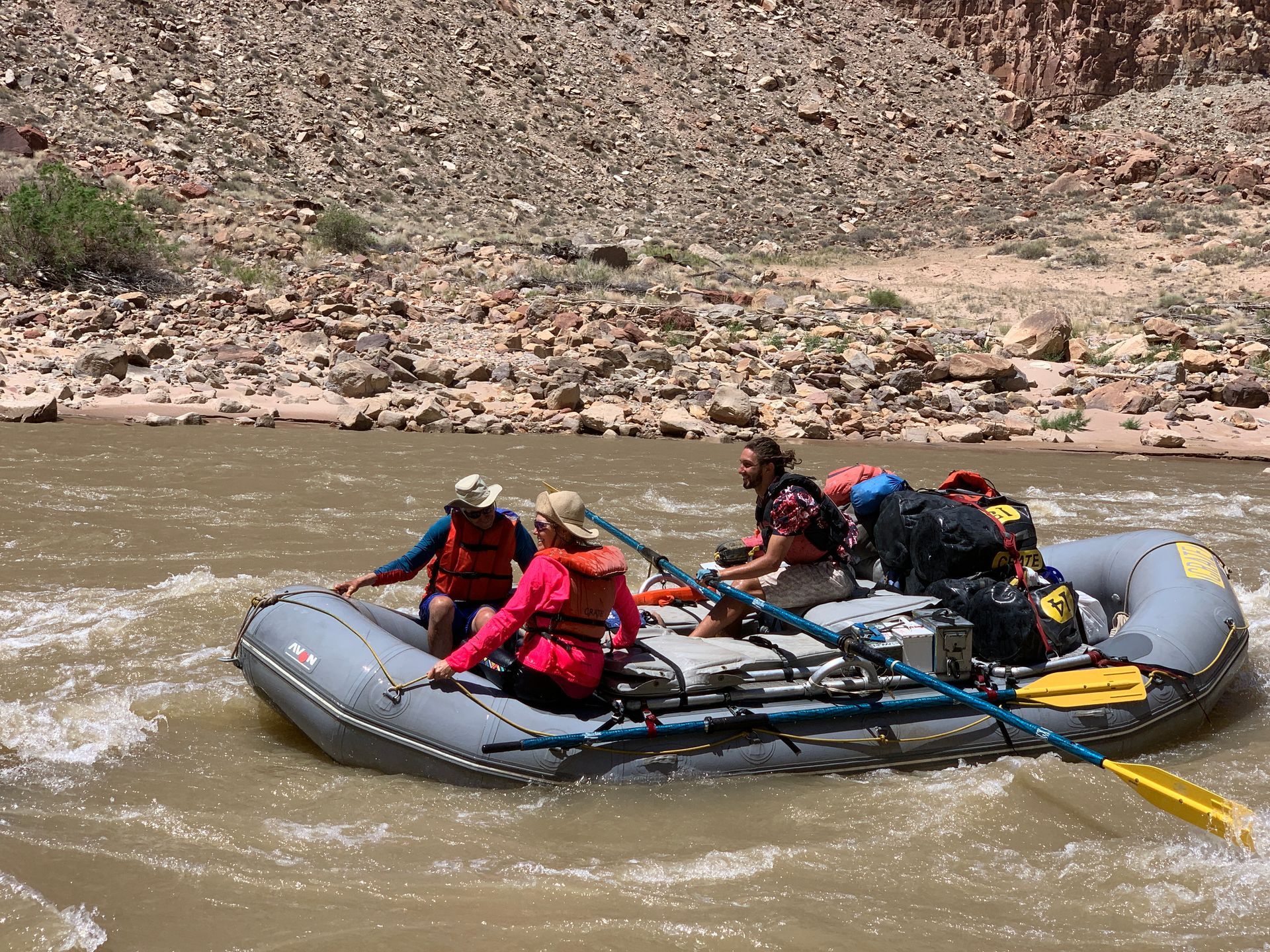 Rafting on a river. Three people in a gray raft navigate white water, rocky canyon background.