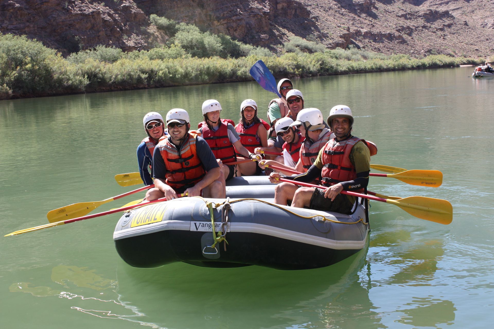 People rafting on a river, wearing life vests and helmets, enjoying a sunny day.