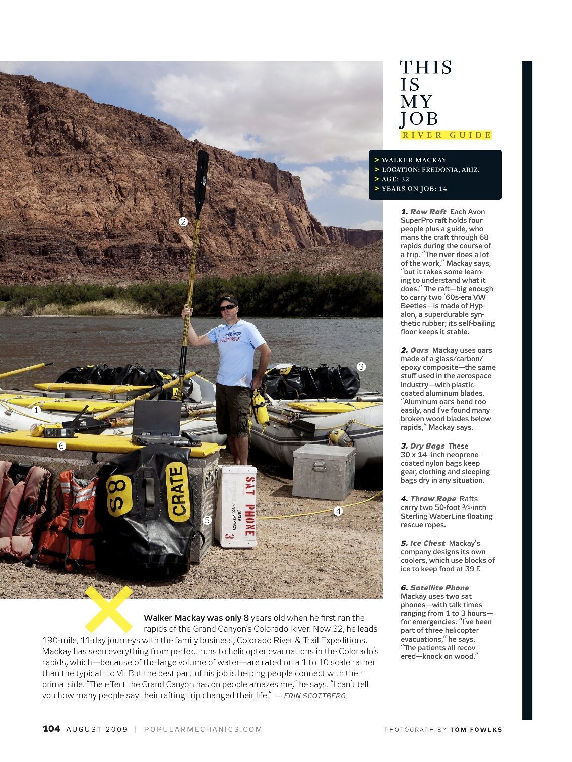 Man in shorts with gear on a riverbank, holding a long pole. Desert backdrop.