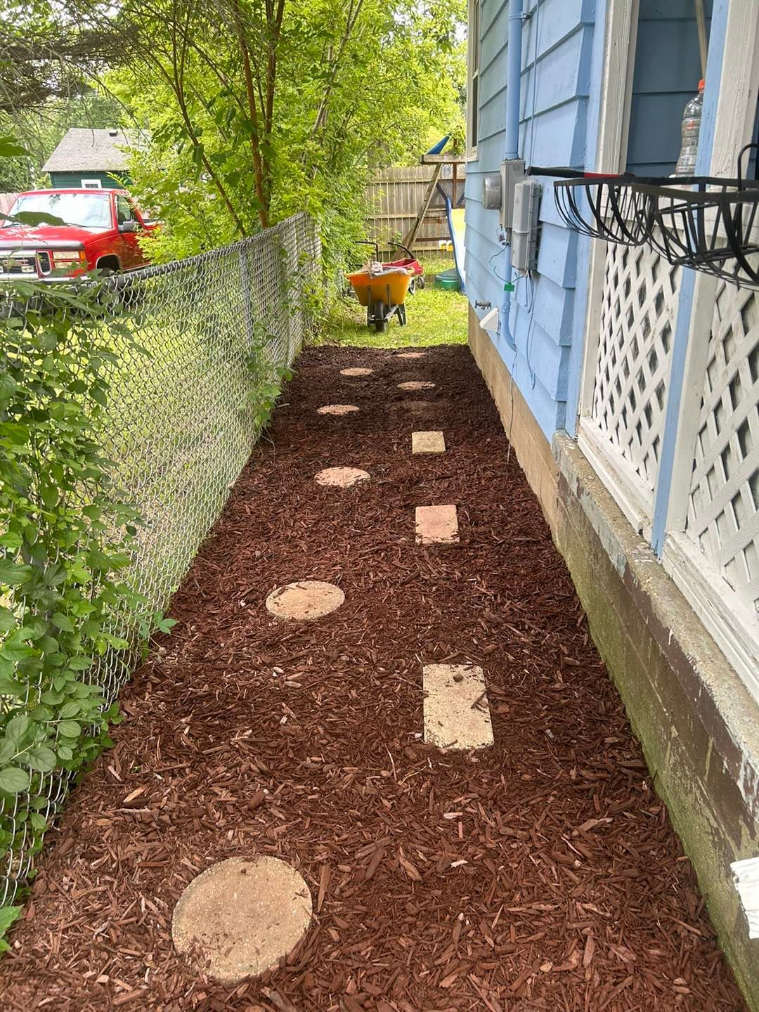 A sidewalk leading to a house with a wheelbarrow in the background.