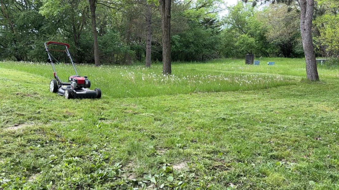 A lawn mower is cutting a lush green lawn in a park.