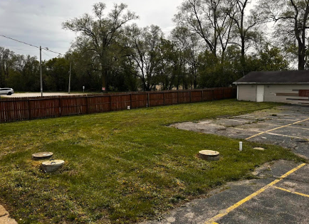 A parking lot with a fence and a house in the background.
