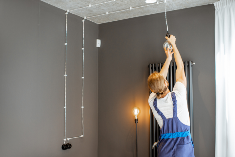 A man is hanging a light bulb from the ceiling in a room.