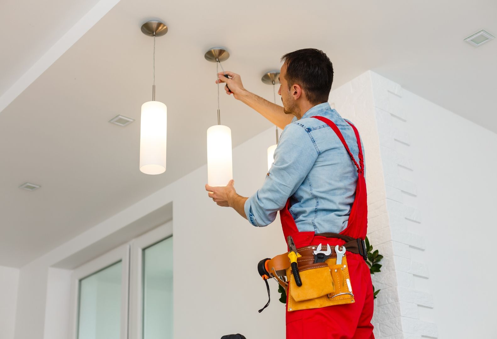 A man is installing a light fixture on the ceiling.