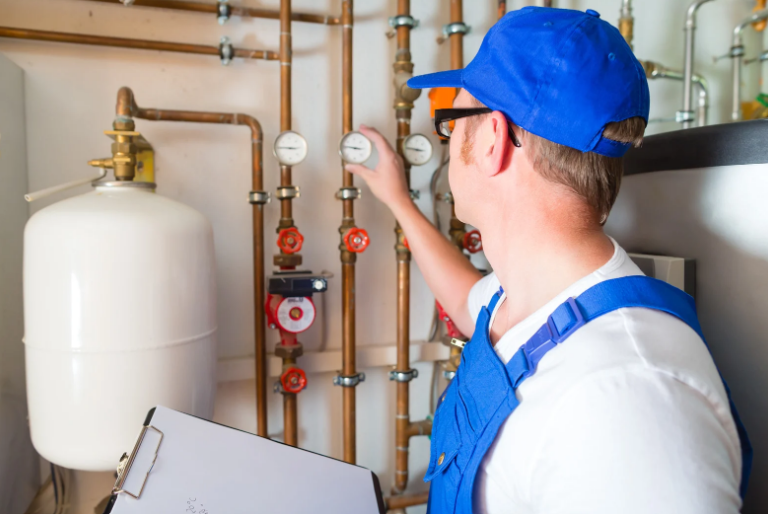A man in a blue hat is working on a pipe while holding a clipboard.