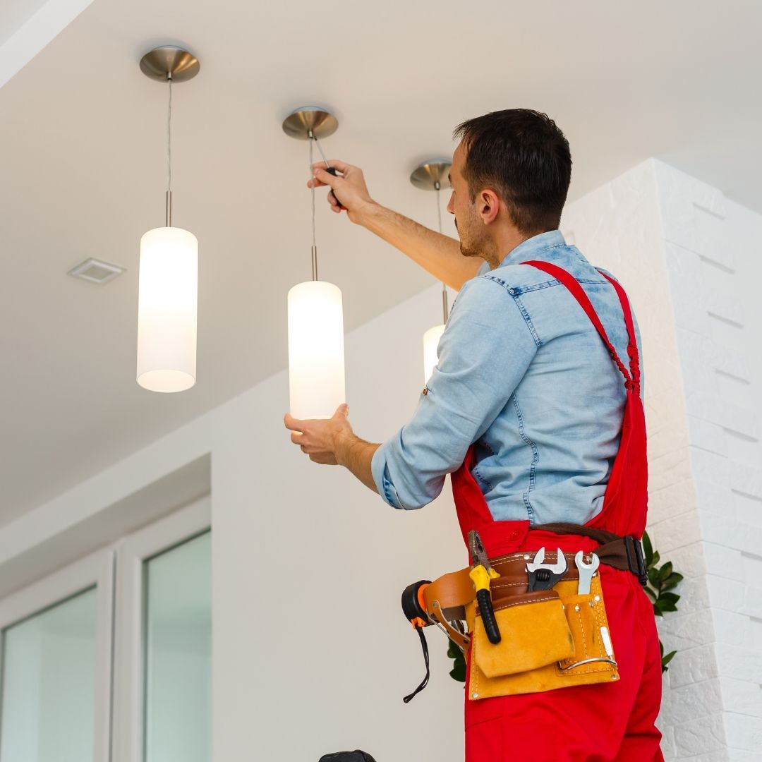 A man in red overalls is working on a light fixture