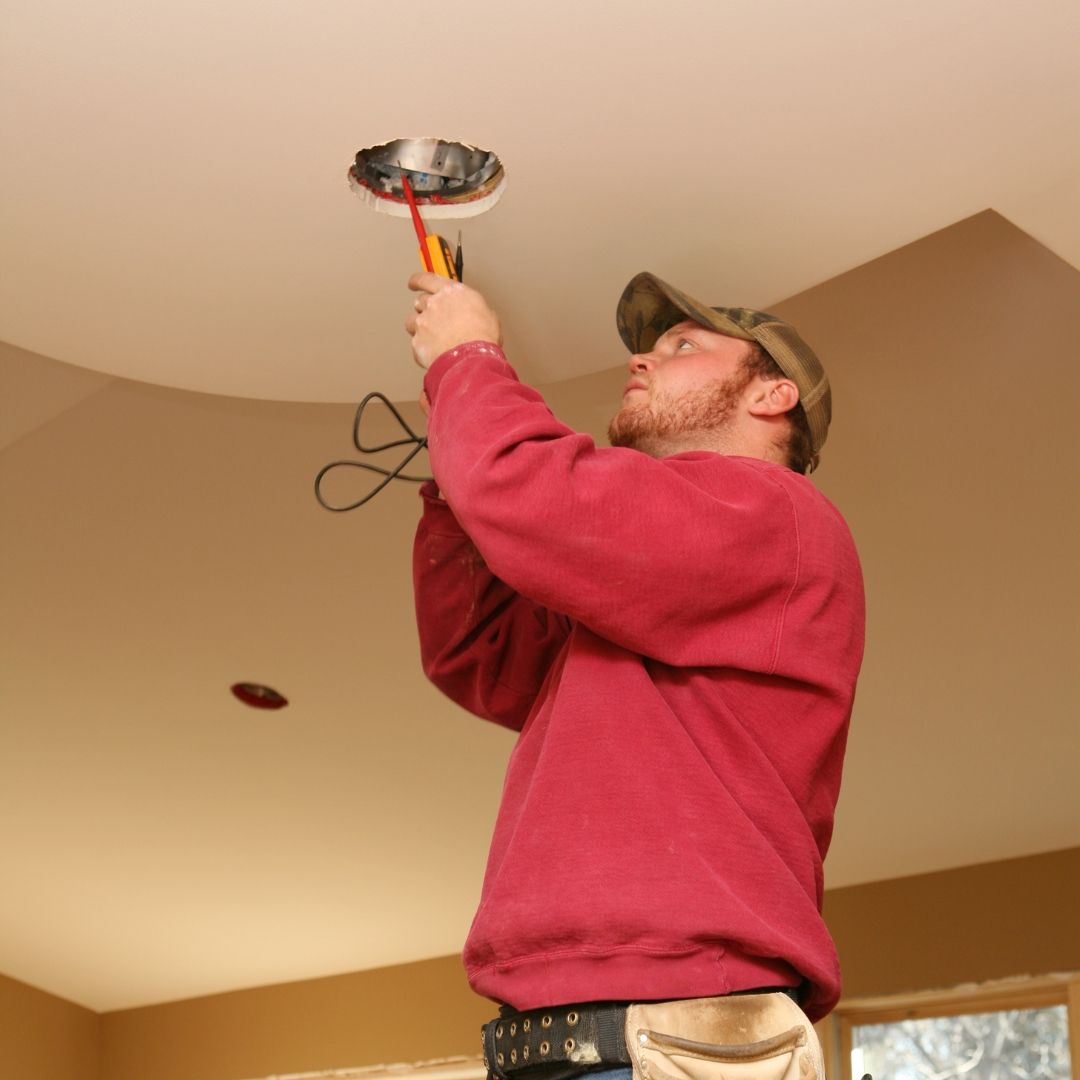 A man in a red sweater is working on a ceiling