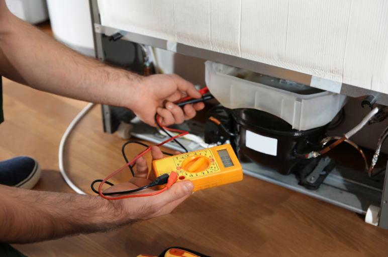 A man is fixing a refrigerator with a multimeter.