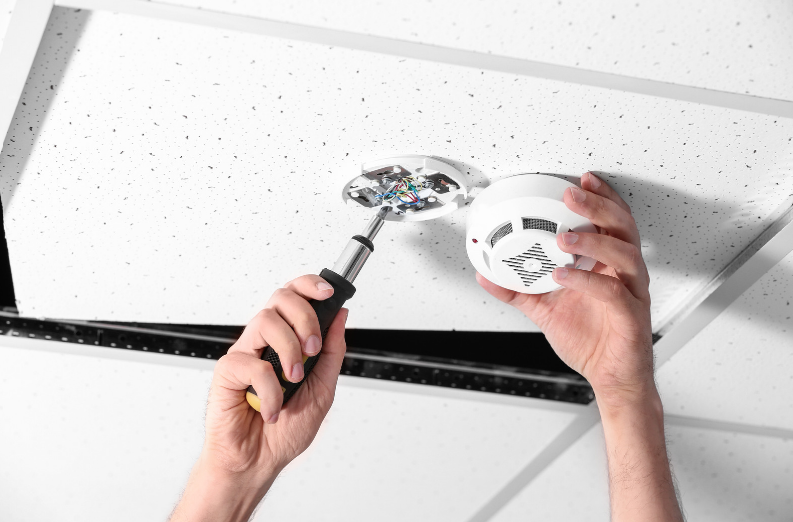 A person is installing a fire alarm on the ceiling.