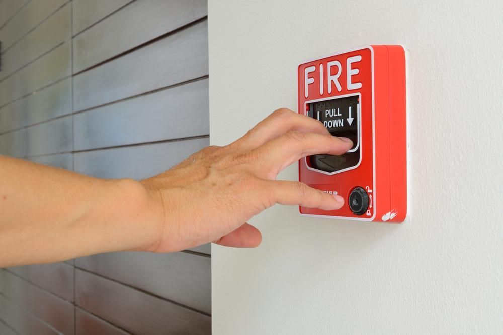 A person is pressing a fire alarm button on a wall.