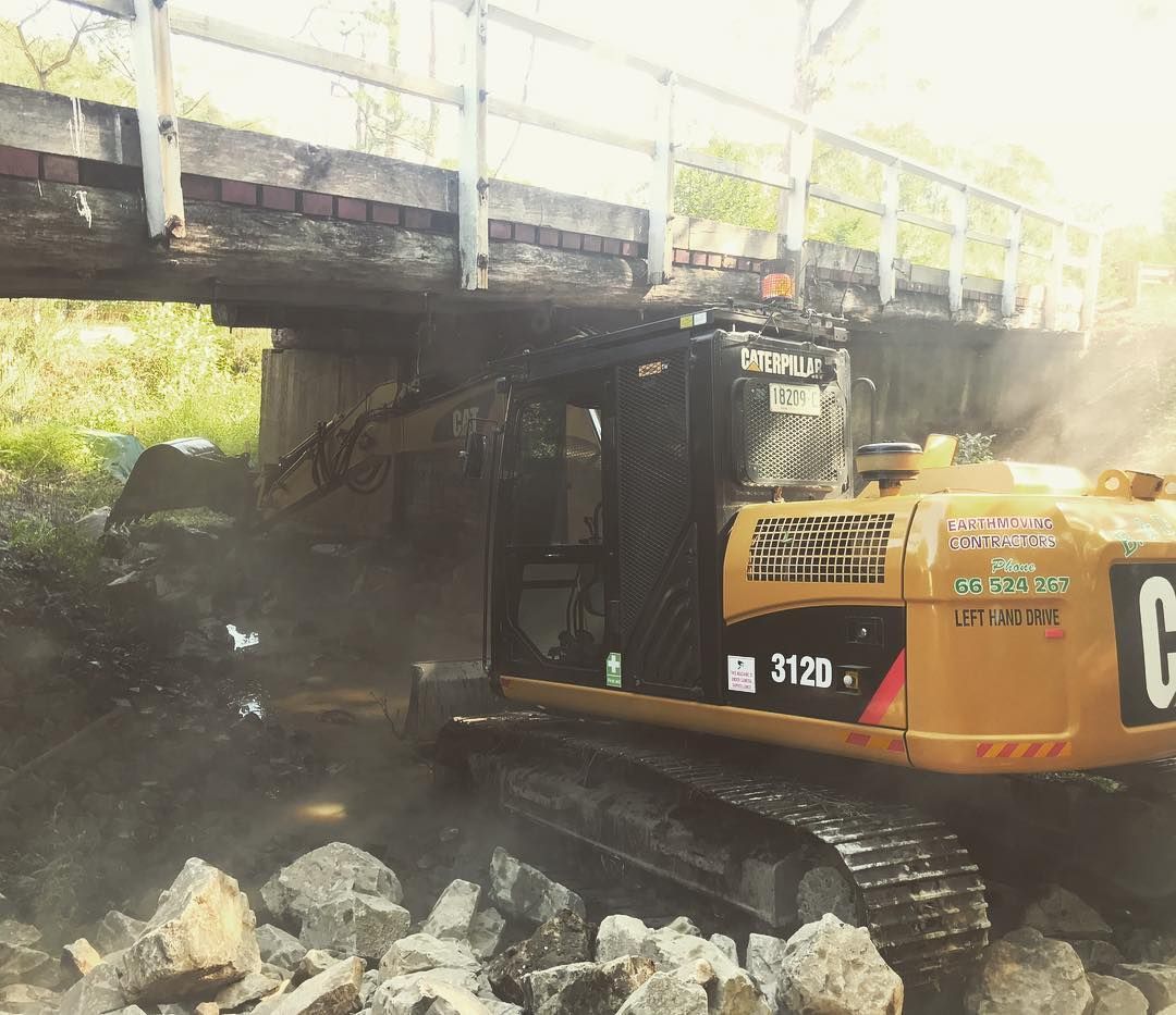 A Yellow Excavator Under a Bridge Removing Debris — B & D Bunt Earthmoving Contractors in North Boambee Valley, NSW