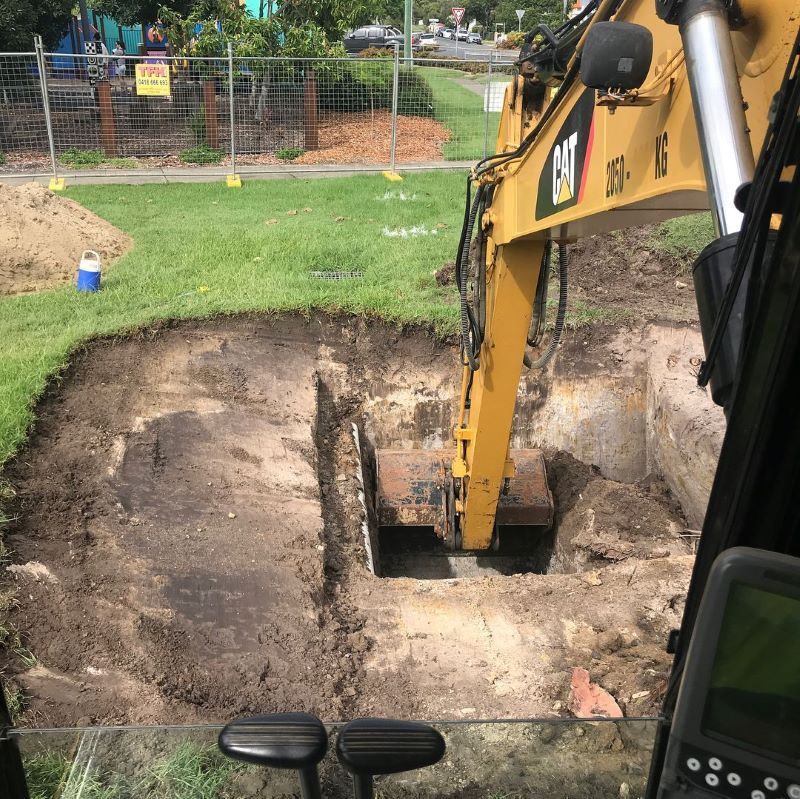 Yellow Excavator Digging a Square Pit in Grassy Area — B & D Bunt Earthmoving Contractors in Grafton, NSW