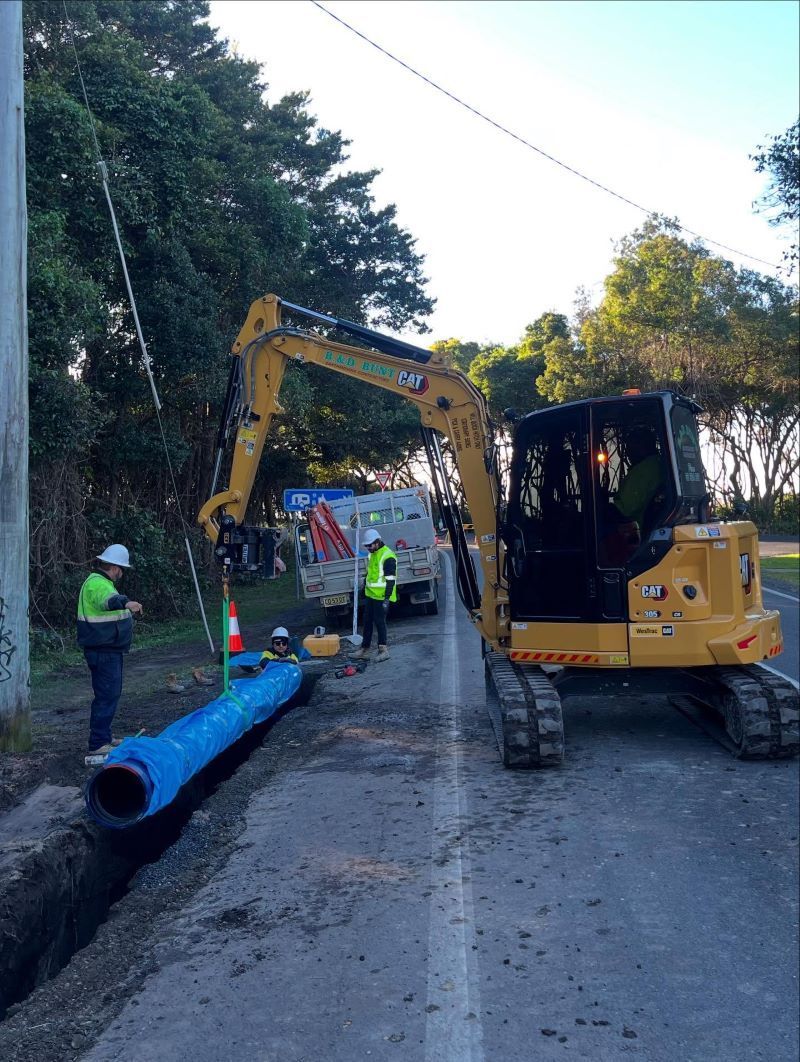 Construction Crew Installing Blue Pipe With an Excavator — B & D Bunt Earthmoving Contractors in North Boambee Valley, NSW