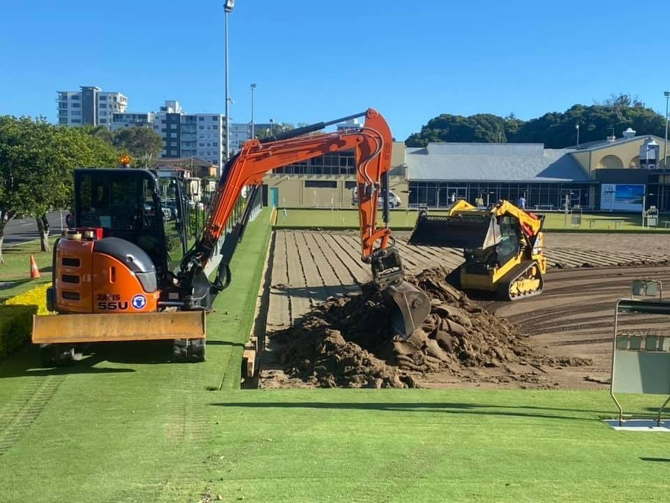 An Excavator and Skid Steer Moving Dirt on a Green Field — B & D Bunt Earthmoving Contractors in North Boambee Valley, NSW