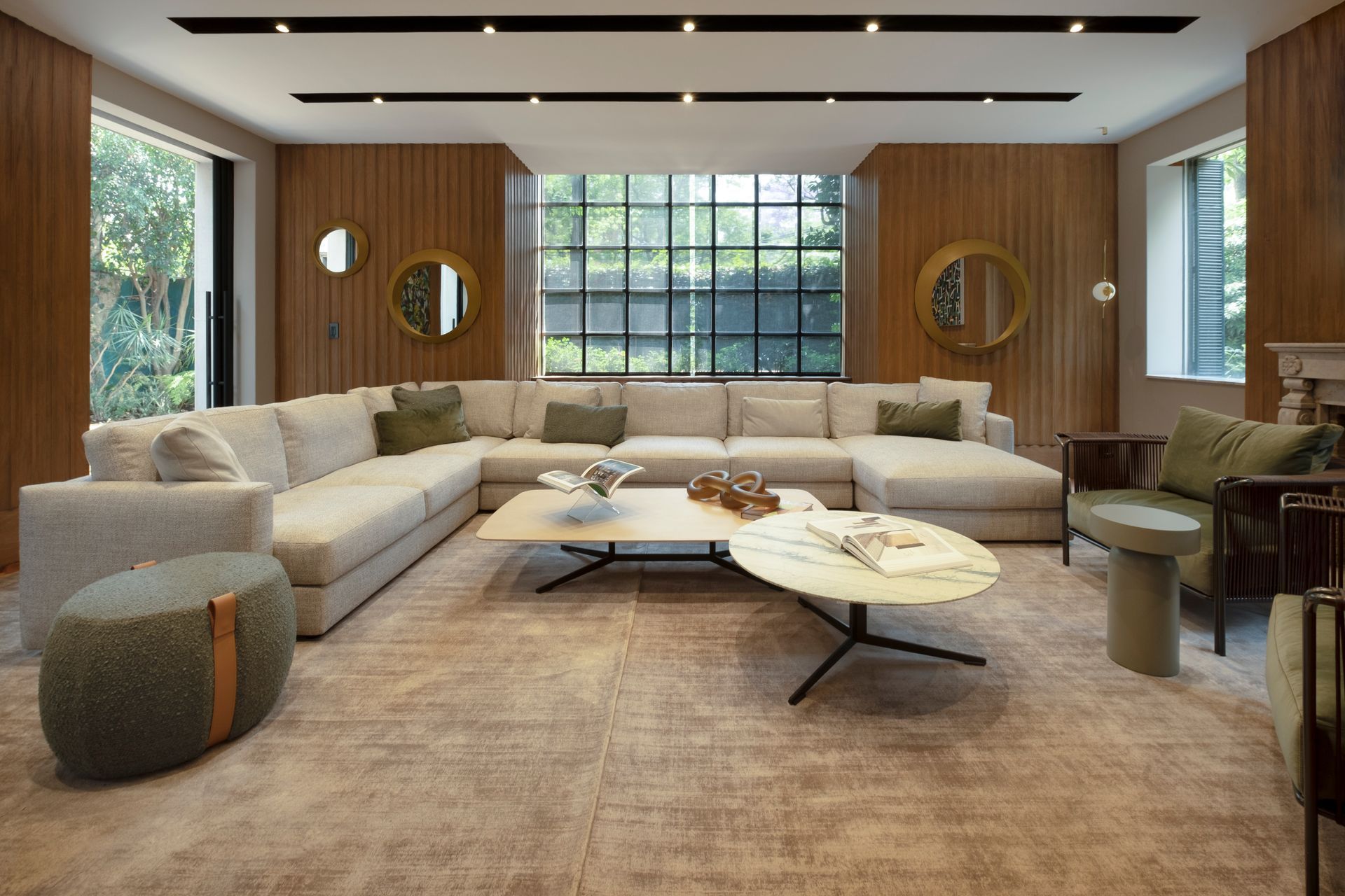 Salón moderno con un gran sofá beige en forma de L, paredes revestidas de madera, una mesa de centro y una mesa ovalada de piedra.