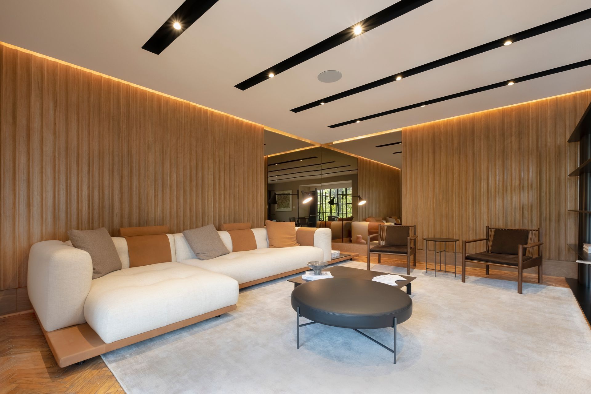 Un salón moderno con paredes revestidas de madera, un gran sofá modular blanco, una mesa de centro redonda oscura y una alfombra.