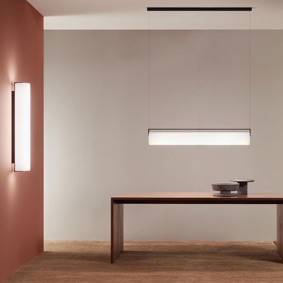 Interior moderno y minimalista con una lámpara colgante lineal sobre una mesa de madera oscura, junto a una lámpara de pared a juego.