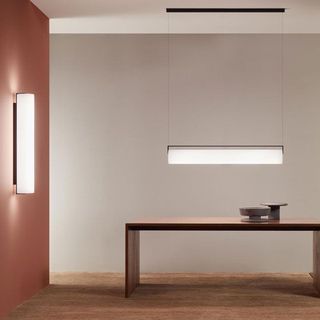 Interior moderno y minimalista con una lámpara colgante lineal sobre una mesa de madera oscura, junto a una lámpara de pared a juego.