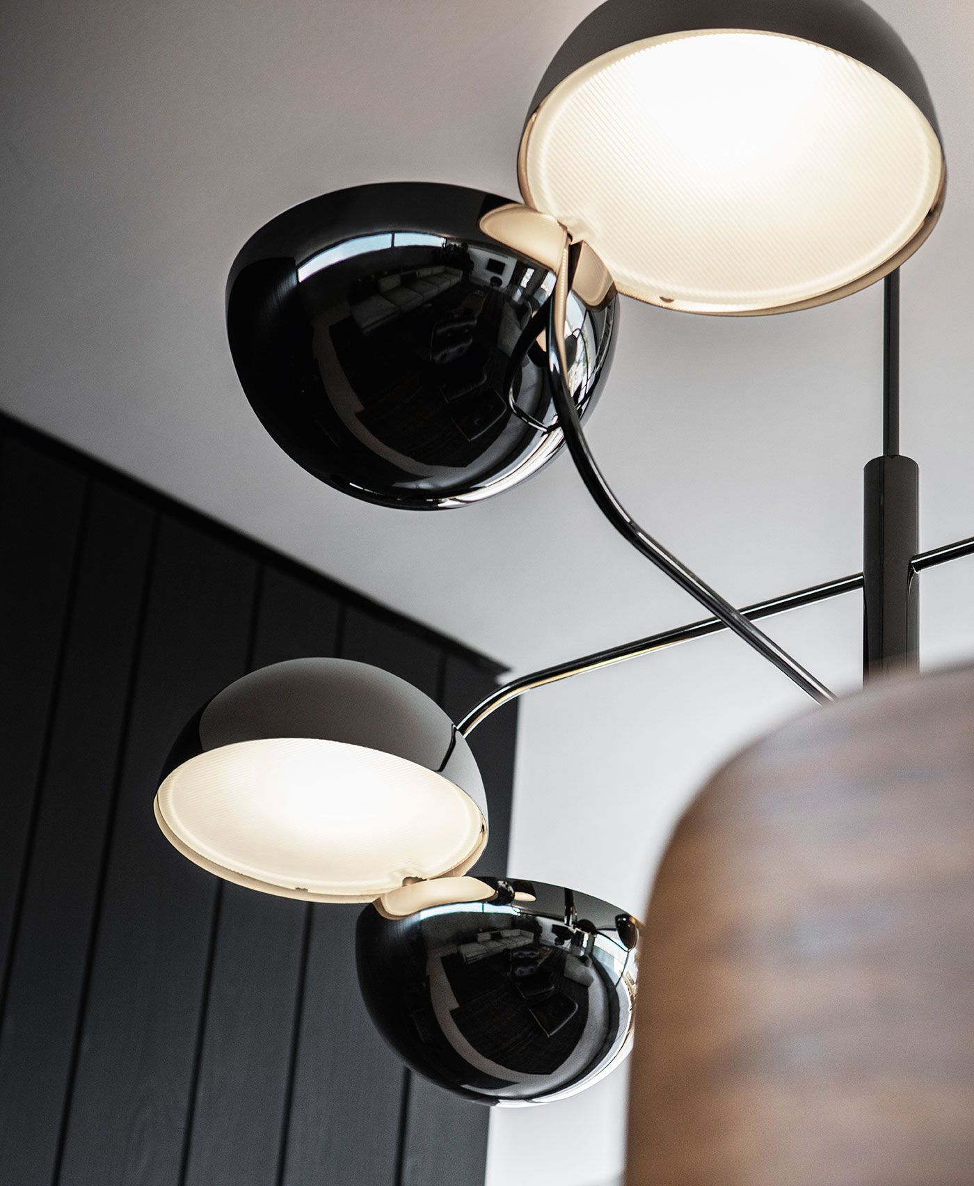 Una moderna lámpara de araña de múltiples brazos con varias pantallas negras brillantes en forma de cuenco que emiten una luz suave y cálida.