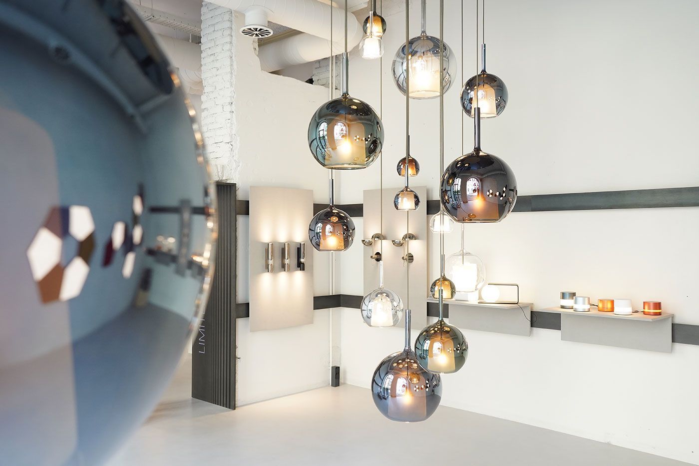 Un conjunto de modernas lámparas colgantes esféricas de cristal reflectante cuelga en una luminosa sala de exposición de iluminación con paredes blancas.
