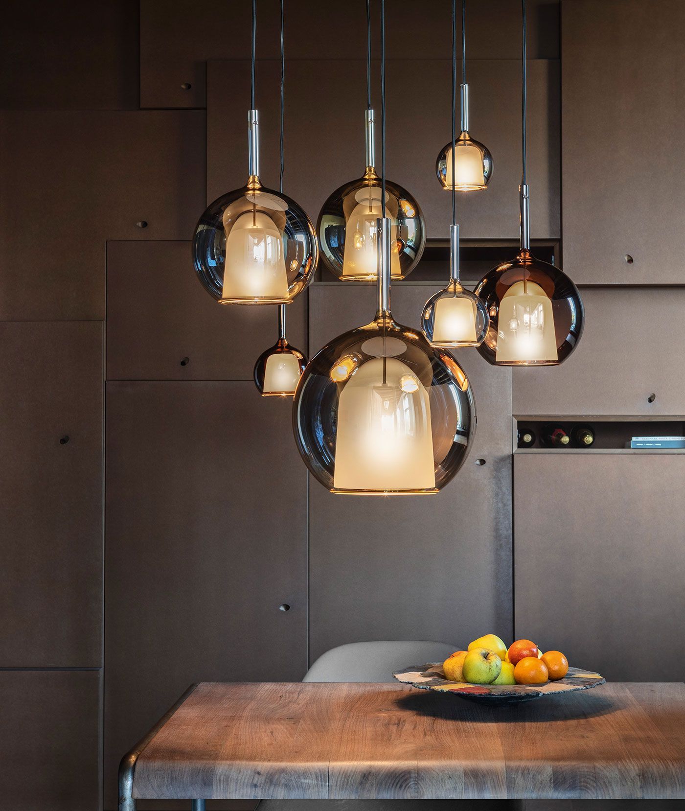 Un conjunto de lámparas colgantes esféricas de cristal color ámbar cuelga sobre una mesa de comedor de madera con un frutero.