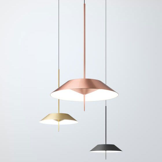 Tres lámparas colgantes minimalistas en cobre, oro y negro cuelgan a diferentes alturas sobre un fondo gris claro.