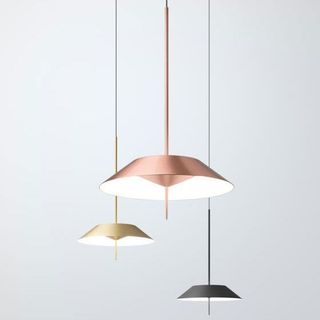 Tres lámparas colgantes minimalistas en cobre, oro y negro cuelgan a diferentes alturas sobre un fondo gris claro.