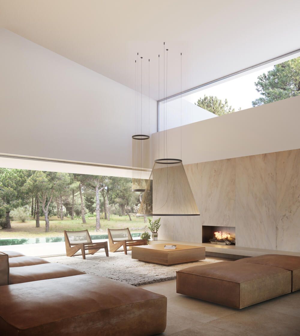 Un salón minimalista con grandes sofás de cuero, dos sillas de madera y una chimenea frente a una ventana panorámica que abarca desde el suelo hasta el techo.