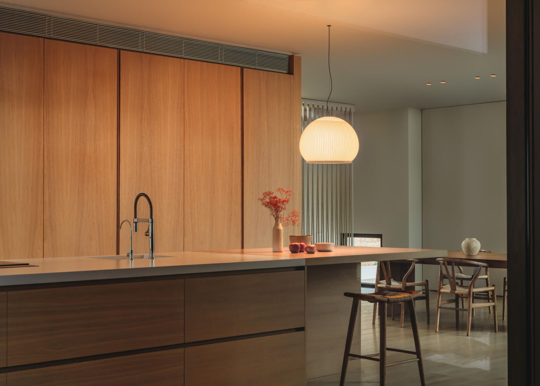 Cocina moderna con armarios de madera, una isla con encimera de color claro, un taburete de bar y una lámpara colgante encima.