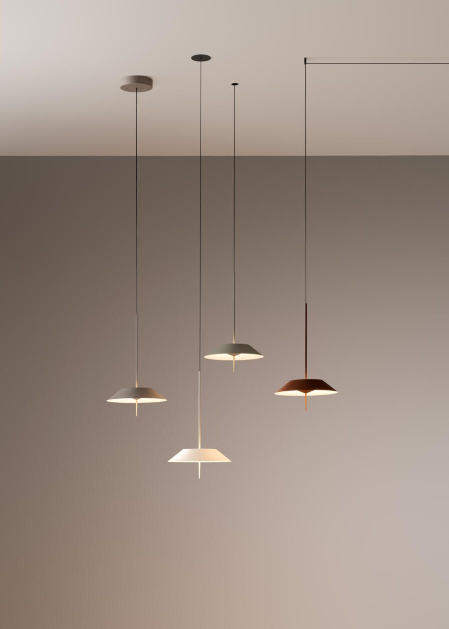 Cuatro modernas lámparas colgantes con tallos delgados y pantallas planas en forma de disco, suspendidas a diferentes alturas contra una pared lisa.