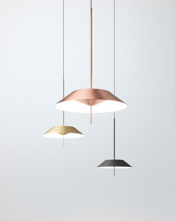 Tres modernas lámparas colgantes en cobre, oro y gris oscuro cuelgan sobre un fondo blanco liso.