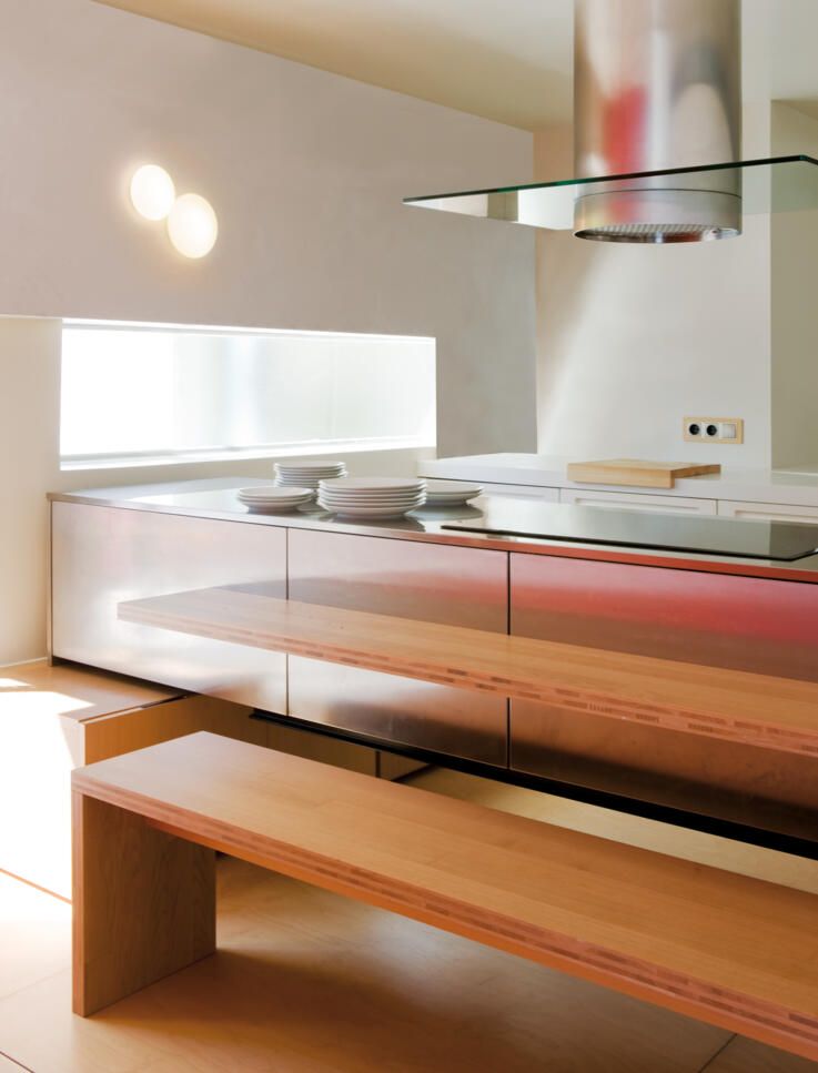 Una cocina moderna con una elegante isla metálica y un banco de madera clara en primer plano.