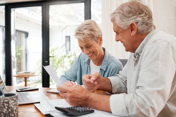 Two people sit at a table reviewing paperwork with a calculator and laptop nearby, looking happy and engaged.