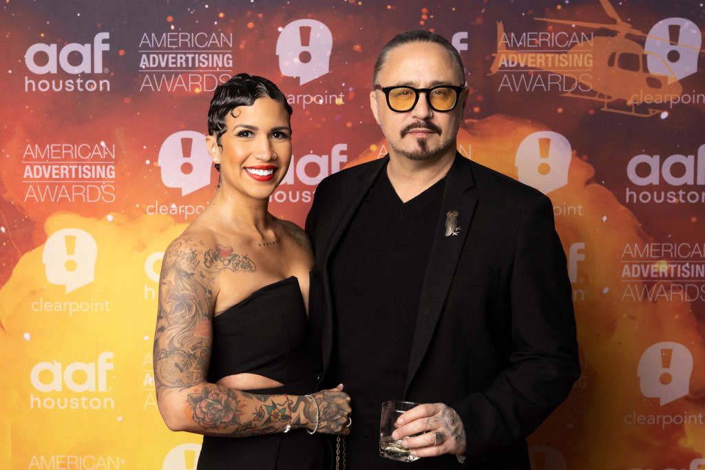 A man and a woman are posing for a picture in front of a wall that says american advertising awards.