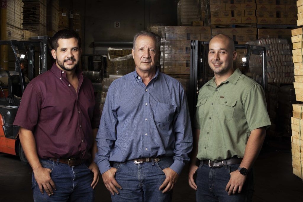 Three men are posing for a picture in a warehouse.