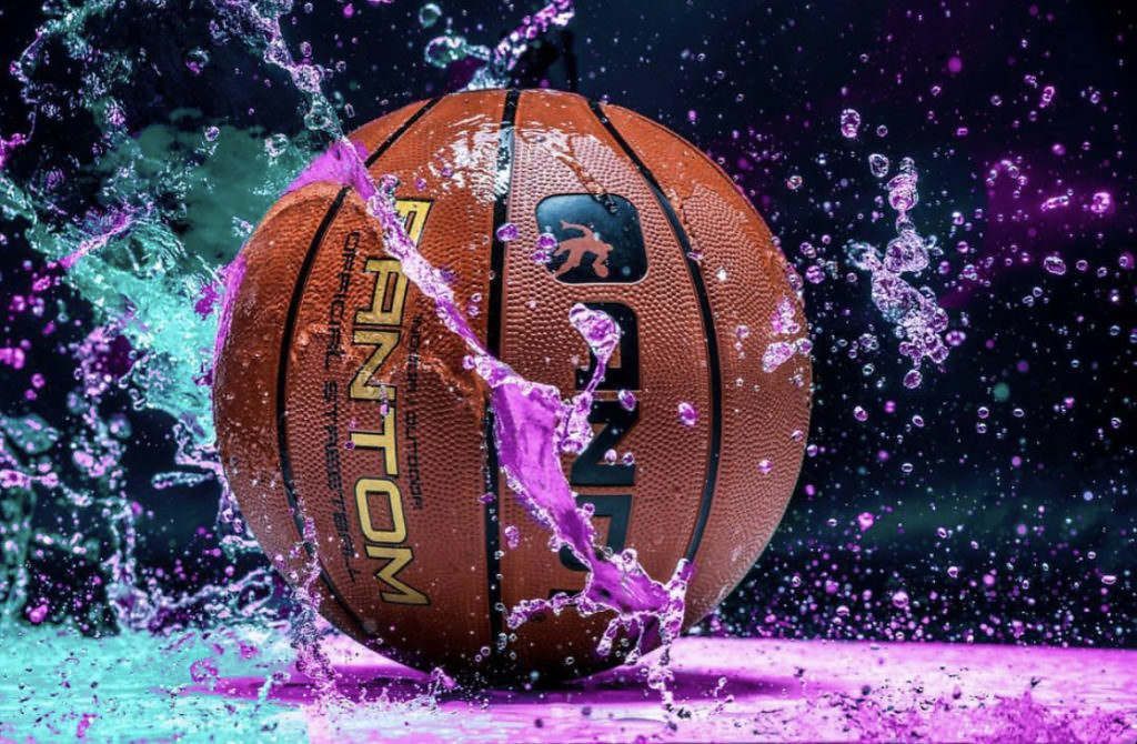 A basketball is being splashed with water on a purple surface.
