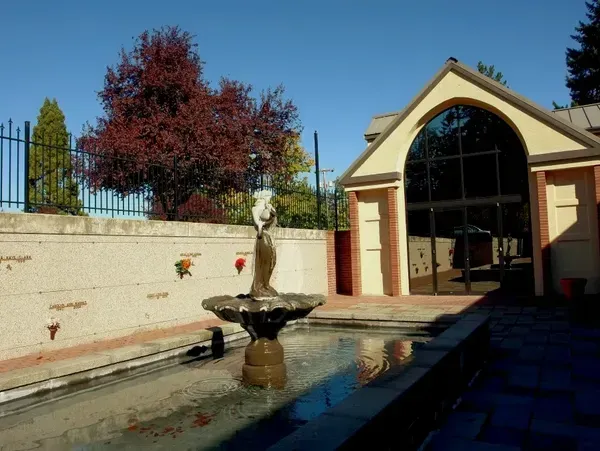 Fountain with statue in front of a building with arched windows and a brick exterior. Red tree, blue sky.