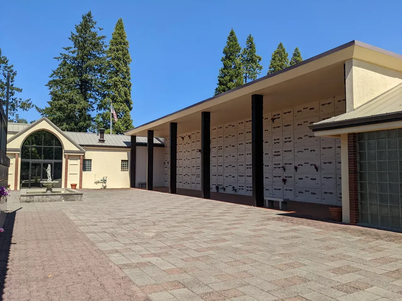 A beige mausoleum with black columns, a brick courtyard, and a fountain in a sunny setting.