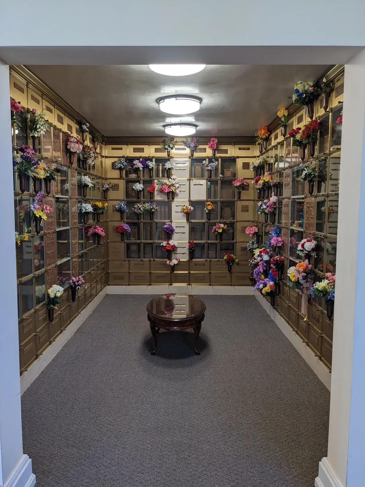 Interior view of a mausoleum with numerous inurnment niches, decorated with floral arrangements.