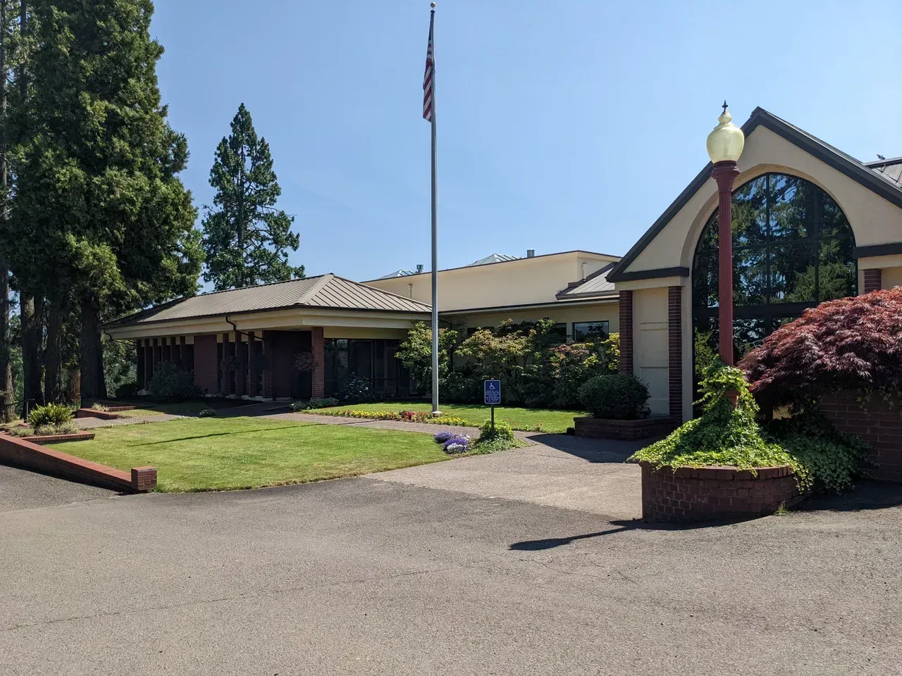 A single-story building with a flag pole and a curved glass window, surrounded by trees and a paved driveway.