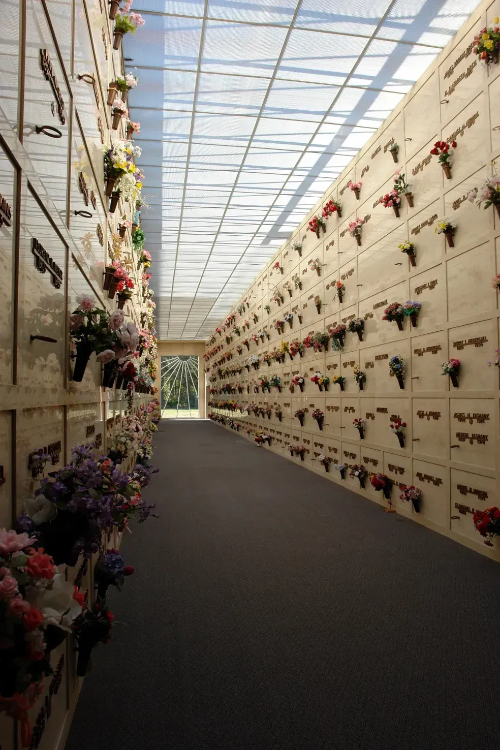 Interior of a mausoleum with rows of crypts decorated with flowers. A skylight illuminates the hallway.