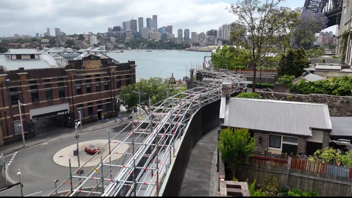 A large swimming pool is surrounded by water and a city in the background.