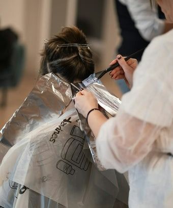 Hairdresser applying highlights to a client's hair in a salon, using a brush and foil.
