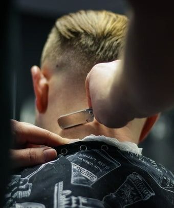 Barber shaves a customer's neck with a straight razor. Close up, showing the barber's hands, neck, and hair.